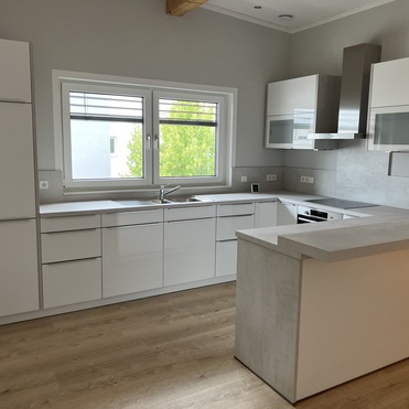 Eine nach Maß gefertigte, moderne Küche mit weißen Schränken, eingebauten Geräten und einer Kochinsel mit hellem Holzboden.