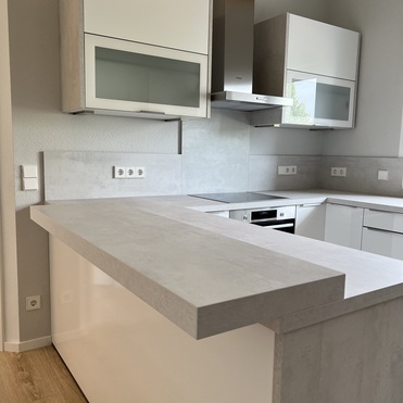 Modern gestaltete Küche nach Maß, mit einer Kombination aus weißen Fronten und einer Kochinsel, unterstrichen durch elegante, graue Akzente.