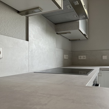 Detailansicht einer maßgeschneiderten Küche mit eingebauter Dunstabzugshaube, Cerankochfeld und diskreten Steckdosen an der Wand.