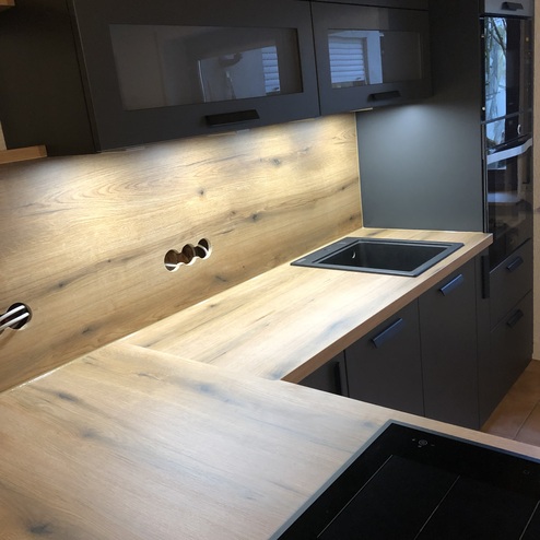 Ansicht einer nach Maß gefertigten Küche mit dunklen Schränken, Holzarbeitsflächen und eingelassenem Spülbecken, stilvoll beleuchtet.