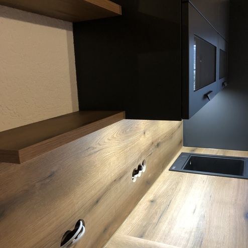 Nahaufnahme einer Küche nach Maß mit Holzarbeitsplatte und dunklen Fronten, ausgestattet mit modernen Griffen und einem Einbauspülbecken.