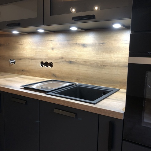 Maßgefertigte Küchenschränke in Dunkelgrau mit integrierter Beleuchtung, Holzakzenten und Einbaugeräten.