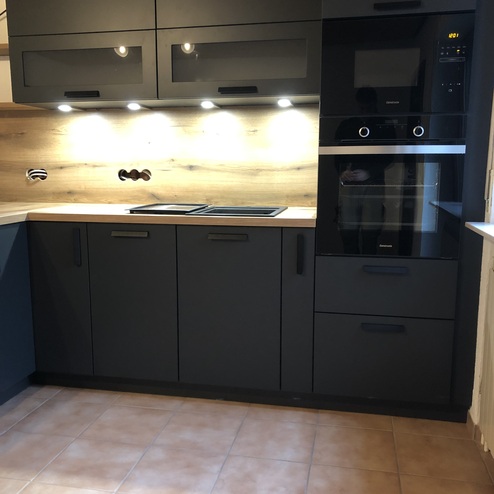 Maßgeschneiderte dunkelgraue Küchenzeile mit eingebautem Backofen, Mikrowelle und Unterbeleuchtung, neben einem Kühlschrank.