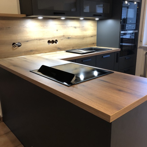 Moderne Küche nach Maß mit einer Insel, glänzender Arbeitsplatte, Kochfeld und stilvoller Holzverkleidung.