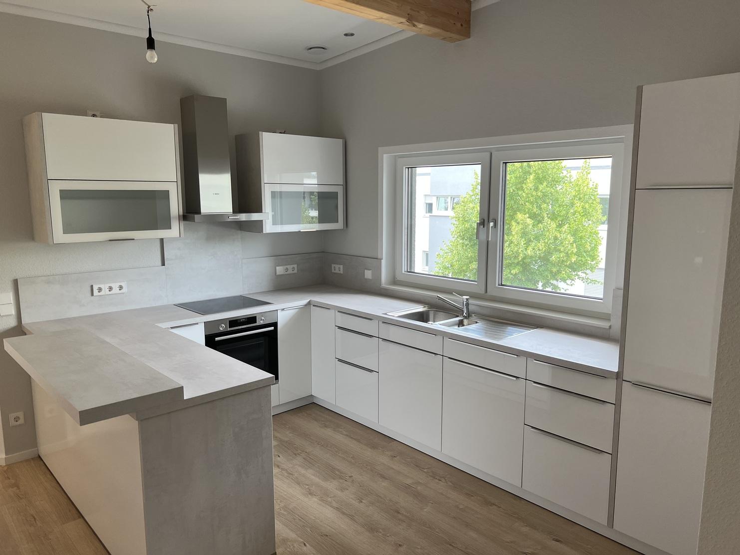 Geräumige, maßgefertigte Küche in Weiß mit modernen Schränken, eingebauten Geräten und einer Kochinsel unter großen Fenstern.