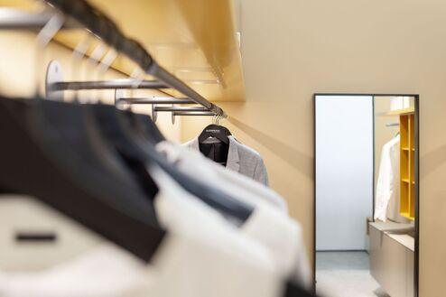 Blick entlang einer offenen Ankleide mit Kleiderstangen, Spiegel und modernem Lichtkonzept von Kallenberger.