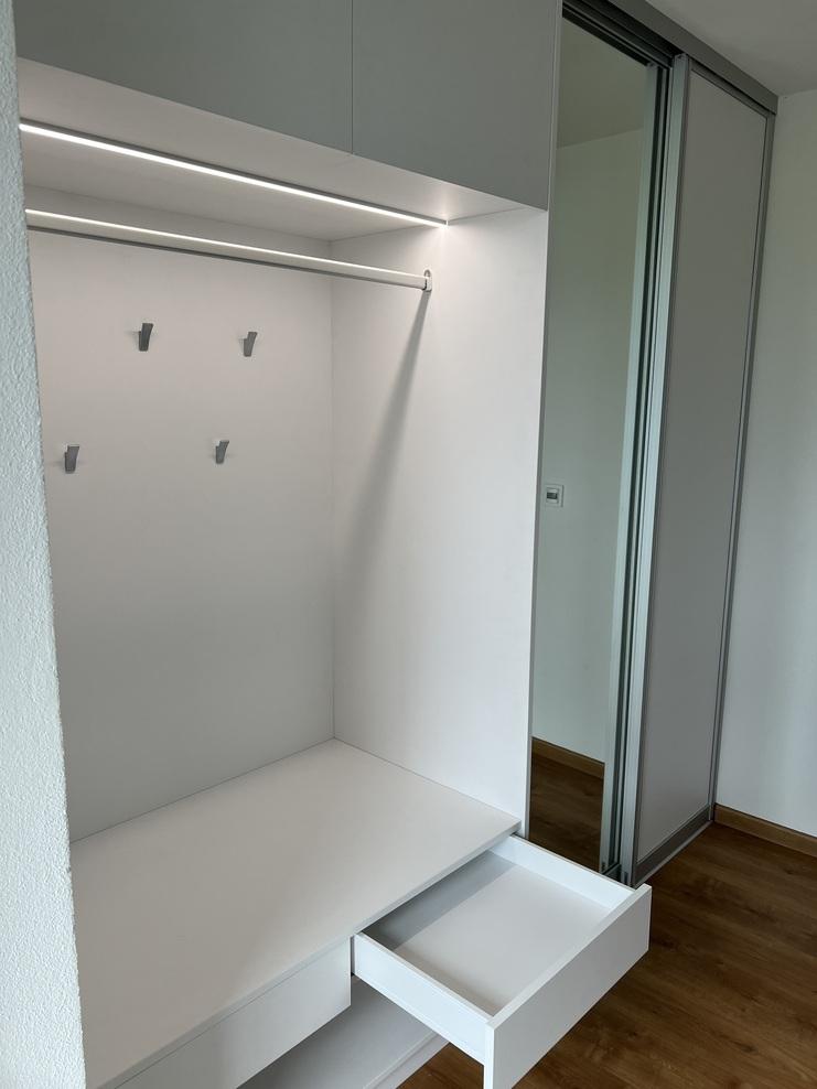 Weiße Garderobe mit Schublade Weiße, minimalistische Garderobe mit Schublade, Kleiderstange und Haken, beleuchtet durch LED-Leiste.